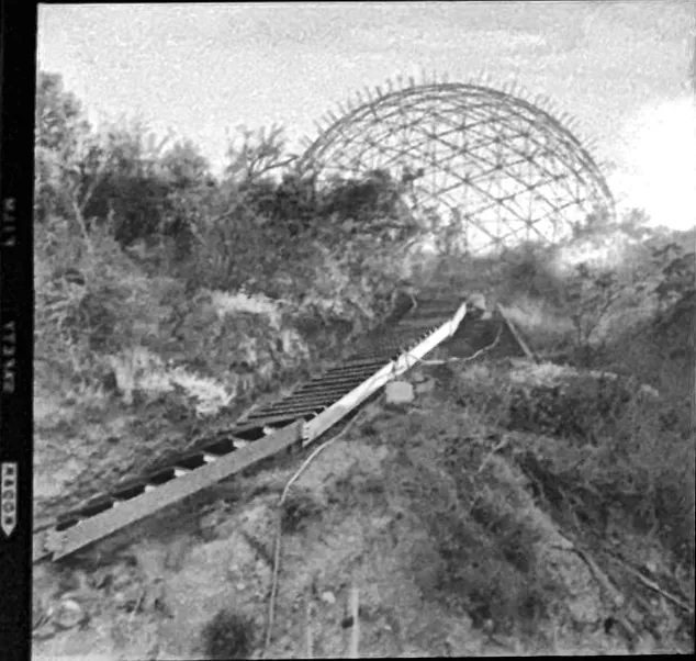 The bare frame on the ridge, with a long timber stair climbing the slope toward it.