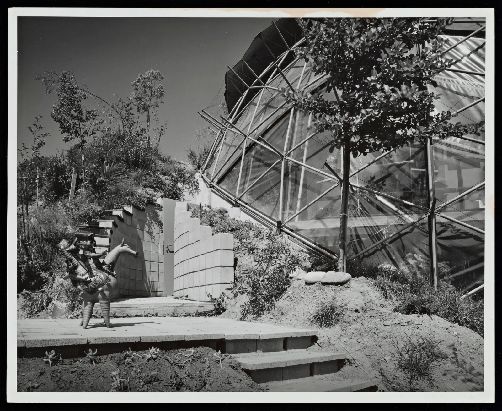 The frame with its skin partly on. A man with a camera stands in the entry court above the block wall and steps.